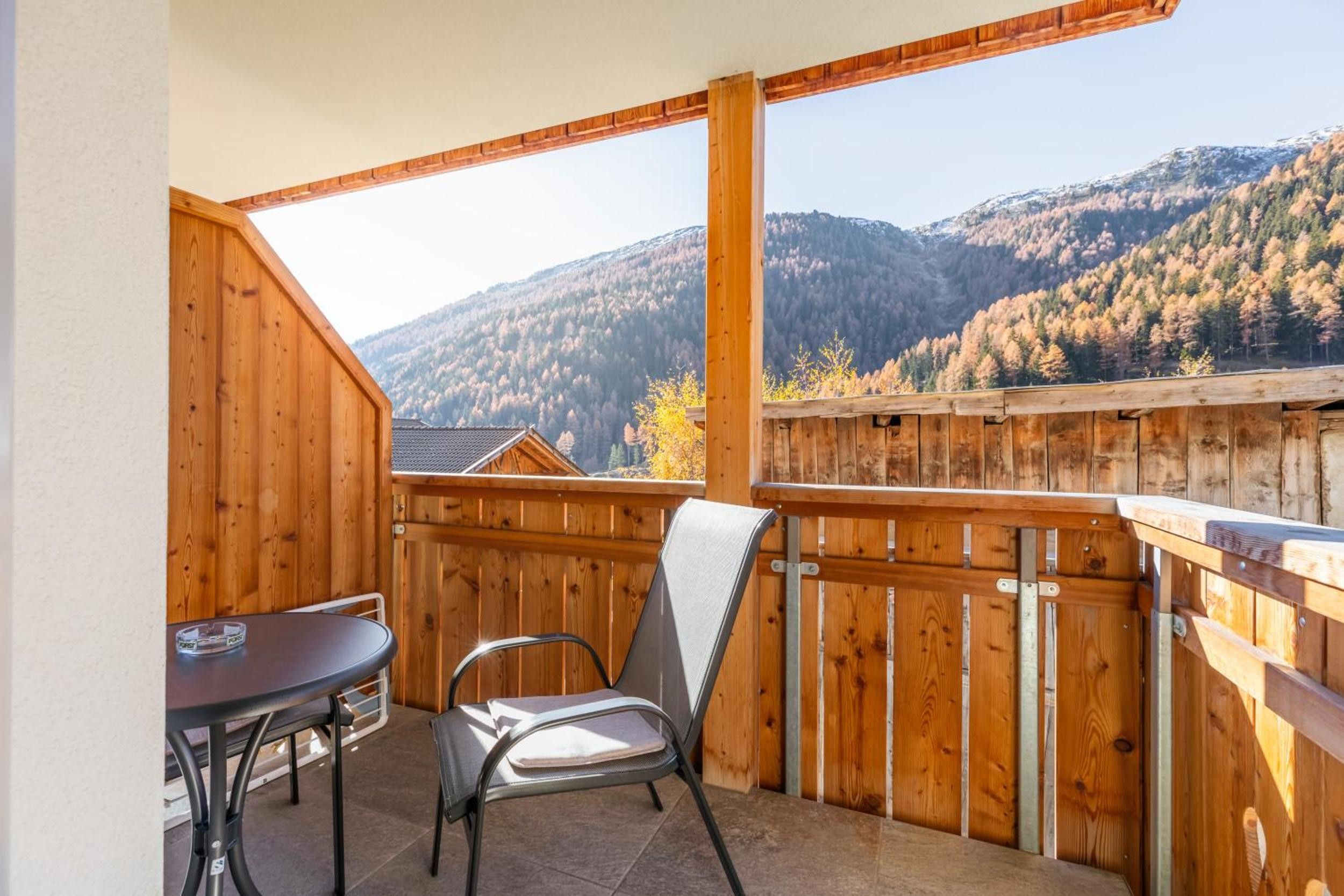 Un balcone in legno con un tavolo e una sedia, affacciato su un paesaggio montuoso.