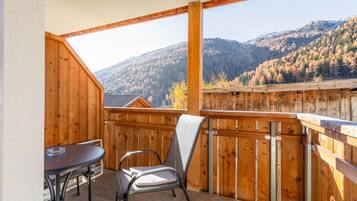 Un balcone in legno con un tavolo e una sedia, affacciato su un paesaggio montuoso.
