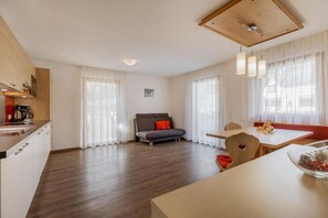 A modern living room with a sofa, a dining table, and a kitchen area with a coffee machine.