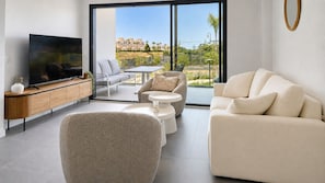 Een moderne woonkamer met een flatscreen televisie, een bank, een salontafel en een eethoek met uitzicht op een woonwijk.