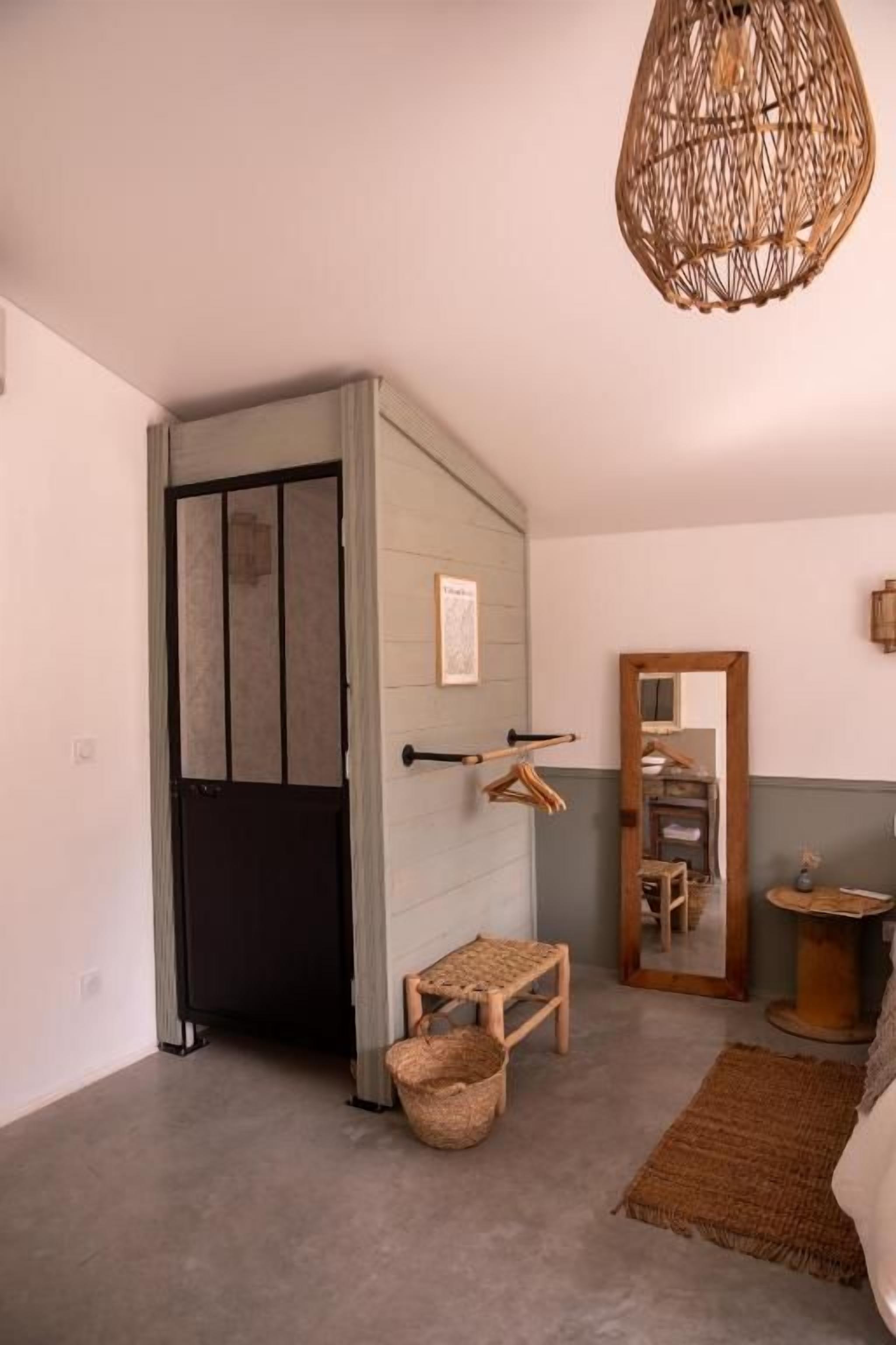 A room with a wardrobe, a hanging rack, a small stool, a woven basket, and a woven rug.
