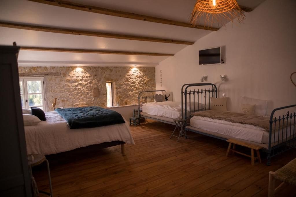 A room with three beds, a stone wall, wooden beams, and a hanging light fixture.