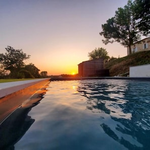 Una piscina con vista al atardecer, rodeada de árboles y un edificio.