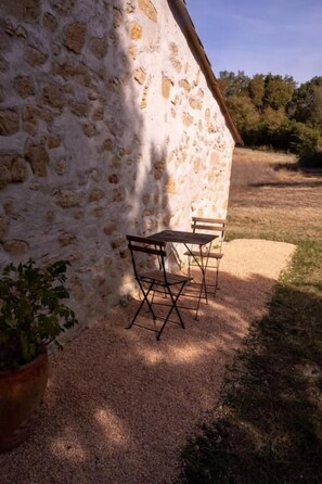 A stone wall with a table and chairs outside, gravel ground, and a potted plant.
