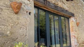 Un bâtiment en pierre doté d’une grande fenêtre et d’une porte, d’une petite table et d’une plante en pot.