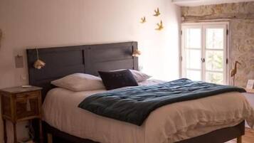 Une chambre avec un plancher en bois, une tête de lit sombre, un lit recouvert de draps blancs et une table de chevet avec une lampe.