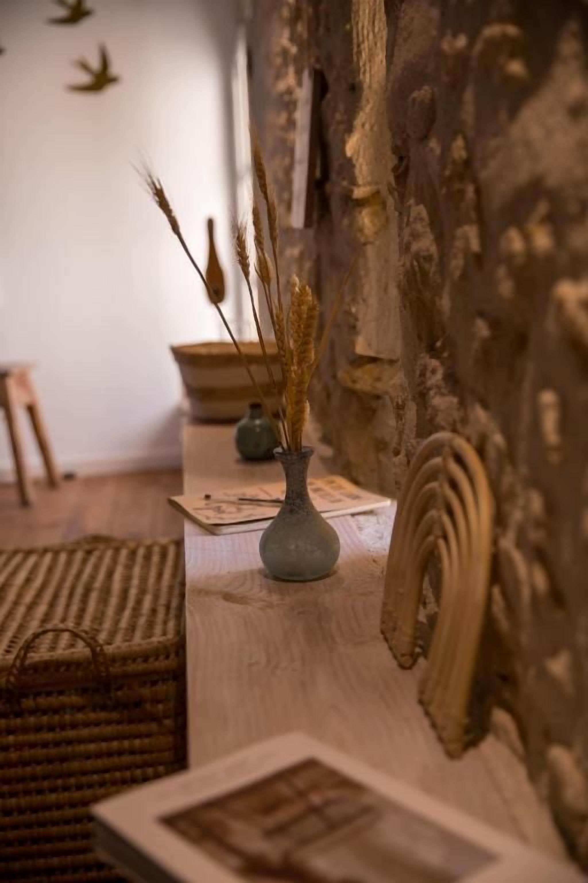 Un intérieur rustique avec une table en bois, un vase contenant des plantes séchées et un mur à la texture particulière.