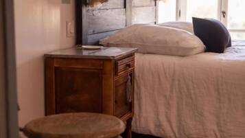 A bedroom with a wooden headboard, a bed with white bedding, a wooden nightstand with books, and a window with curtains.