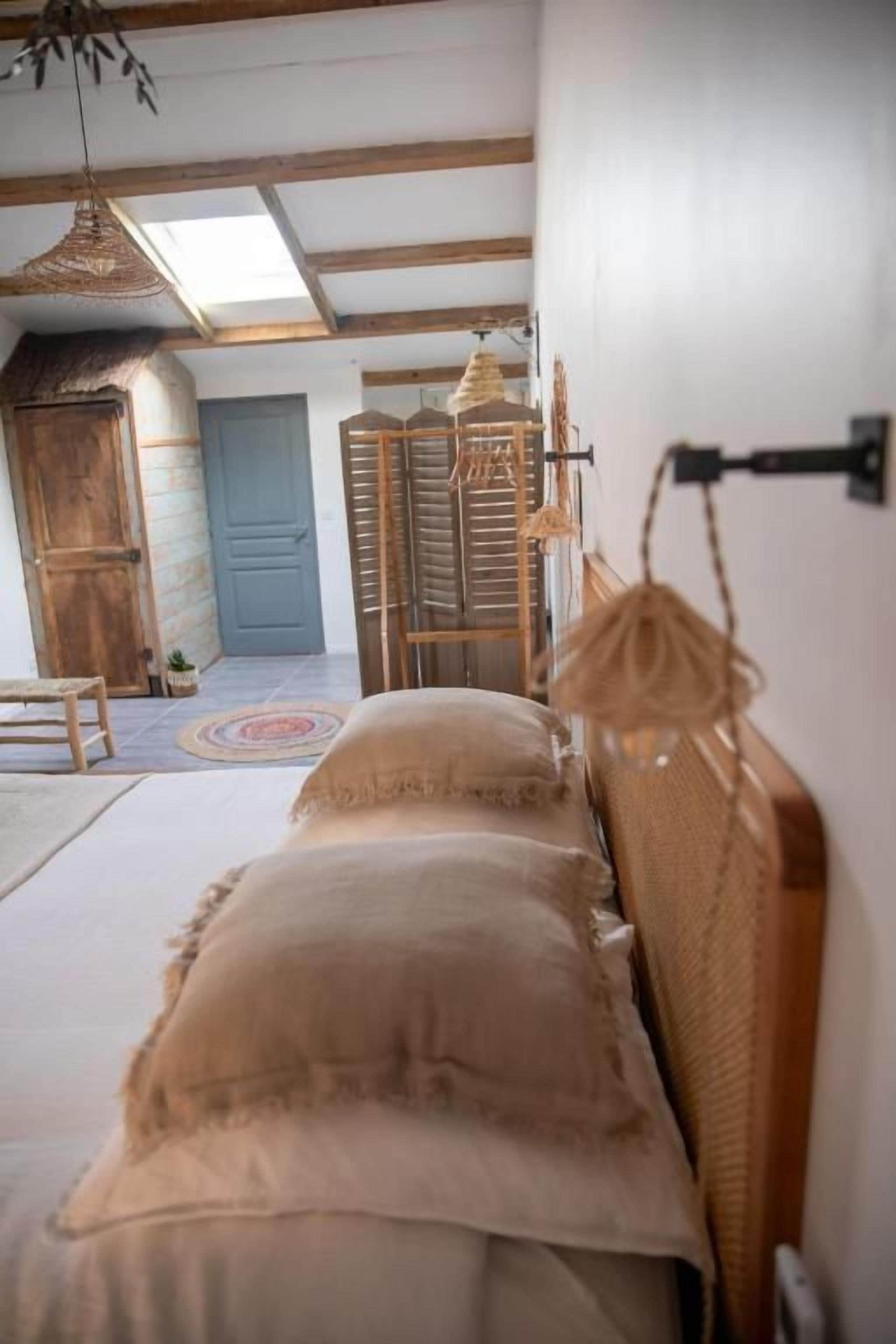 A bed with a wooden headboard, a hanging light fixture, and a view of a blue door and a wooden cabinet in the background.