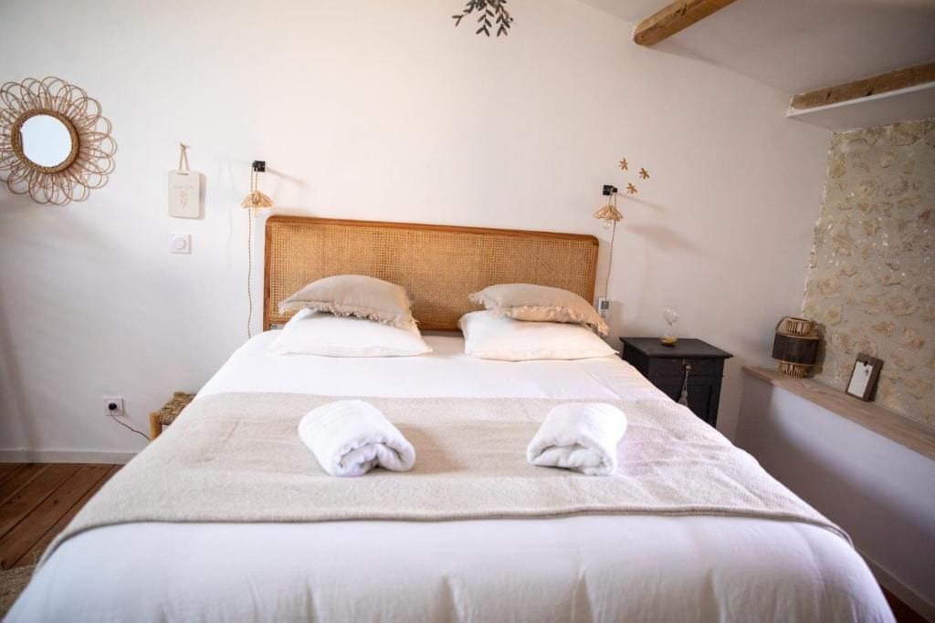 A neatly made bed with two pillows, a bedside table with a lamp, and a wall-mounted mirror.