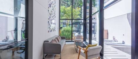 A modern living room with a sofa, chairs, and a dining table. Large windows provide a view of the outdoors.