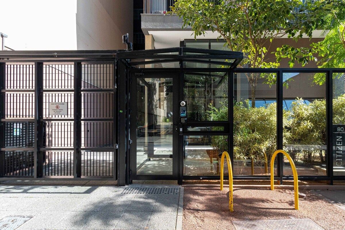 A glass-enclosed entrance with a metal gate, a tree, and a yellow bicycle rack.