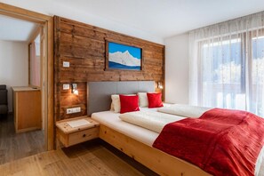 A hotel room with a wooden headboard, a bed with white and red bedding, a nightstand, and a painting of a mountain.
