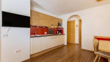 Una cucina compatta con mobili in legno, un forno a microonde integrato e un piano di lavoro rosso.