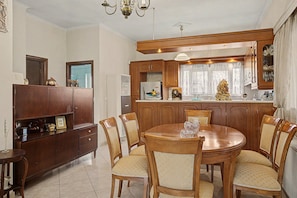 A dining area with a round wooden table and six chairs, a kitchen with wooden cabinets, and a chandelier.