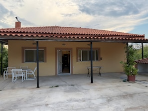 Une maison de plain-pied avec un toit en tuiles, un patio couvert avec une table et des chaises, et une plante en pot.