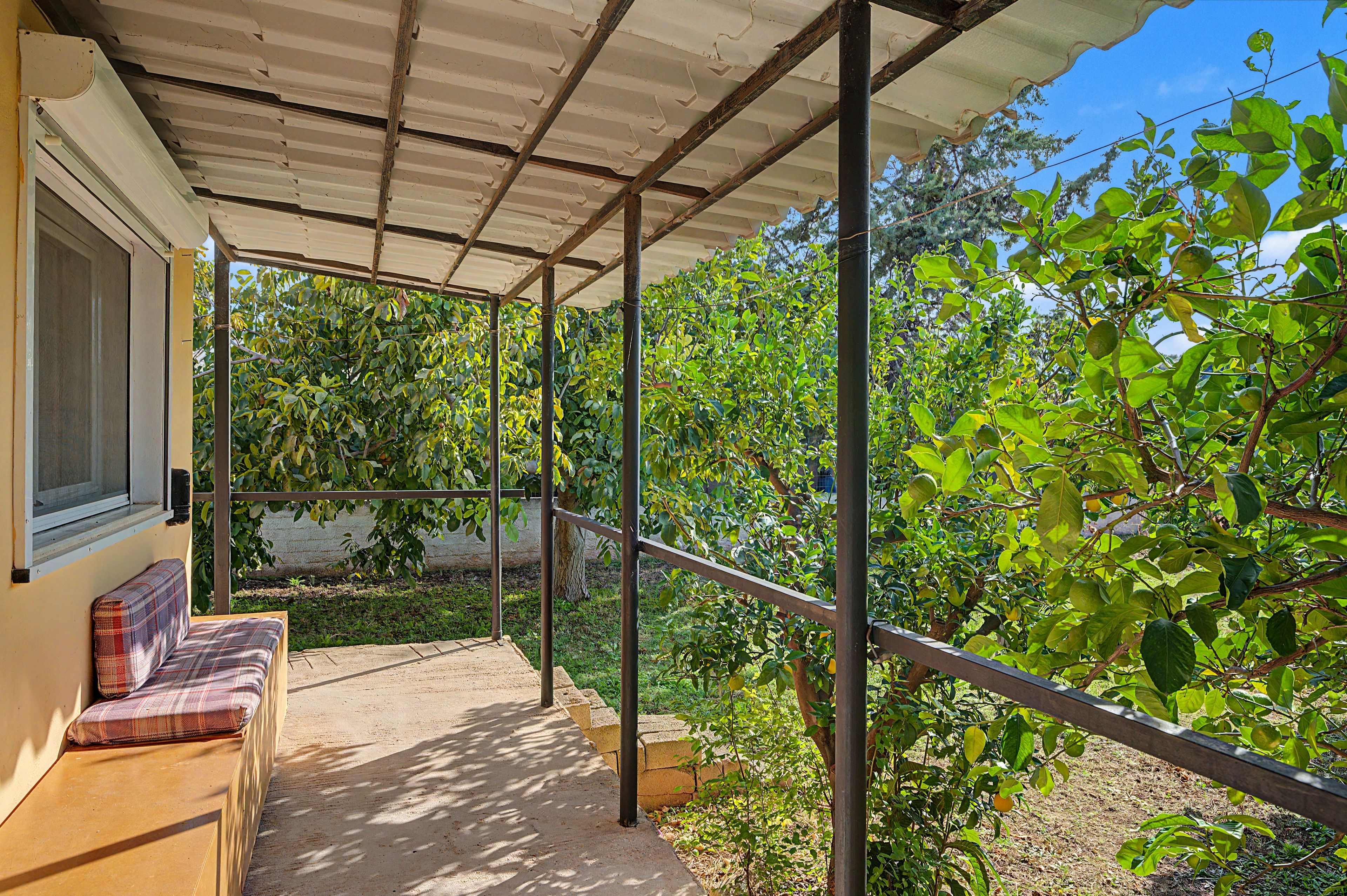 A covered outdoor area with a bench, a window, and a view of a garden with trees and plants.