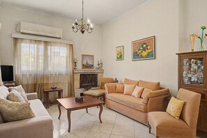 A living room with a sofa, a coffee table, a fireplace, and two paintings on the wall.