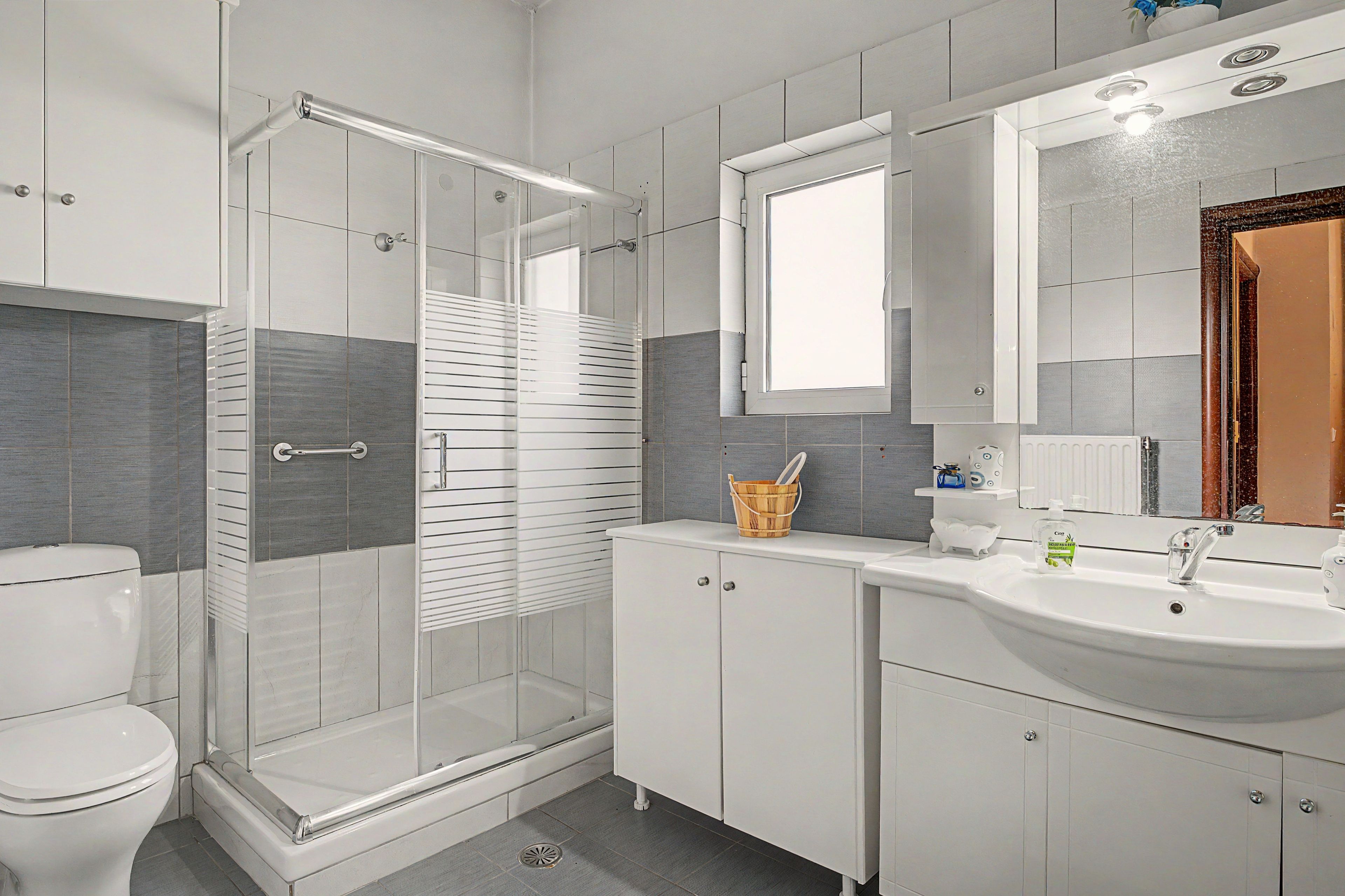 A modern bathroom with a glass shower enclosure, a white toilet, a sink with a mirror above, and a cabinet with a basket.