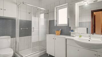 A modern bathroom with a glass shower enclosure, a white toilet, a sink with a mirror above, and a cabinet with a basket.