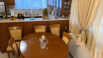 En matplats med ett träbord och stolar, en kristallkrona och ett fönster med gardiner.