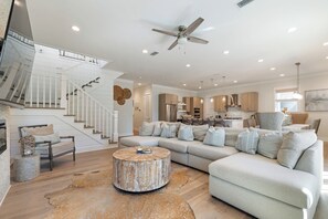 A spacious living room with a large sectional sofa, a round coffee table, and a staircase with white railings. - Out of Office Beaches | Lagoon Pool, 7 Bikes, Screened Balcony, Sleeps 14 (Seacrest Beach)