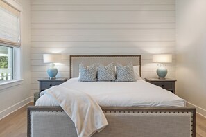 Une chambre à coucher avec un grand lit, deux tables de chevet avec des lampes et une fenêtre avec des stores.