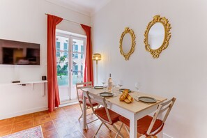 Een eetruimte met een tafel gedekt voor twee personen, een aan de muur bevestigde televisie en twee sierlijke spiegels.