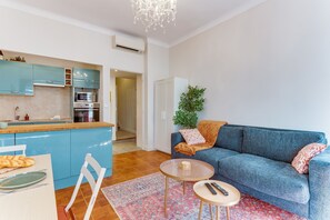 A modern living room with a blue sofa, a small coffee table, and a kitchen area with blue cabinets and a microwave. - THE LIBERTY AP4510 - Clim - 5-6 min de la plage by (Nice)