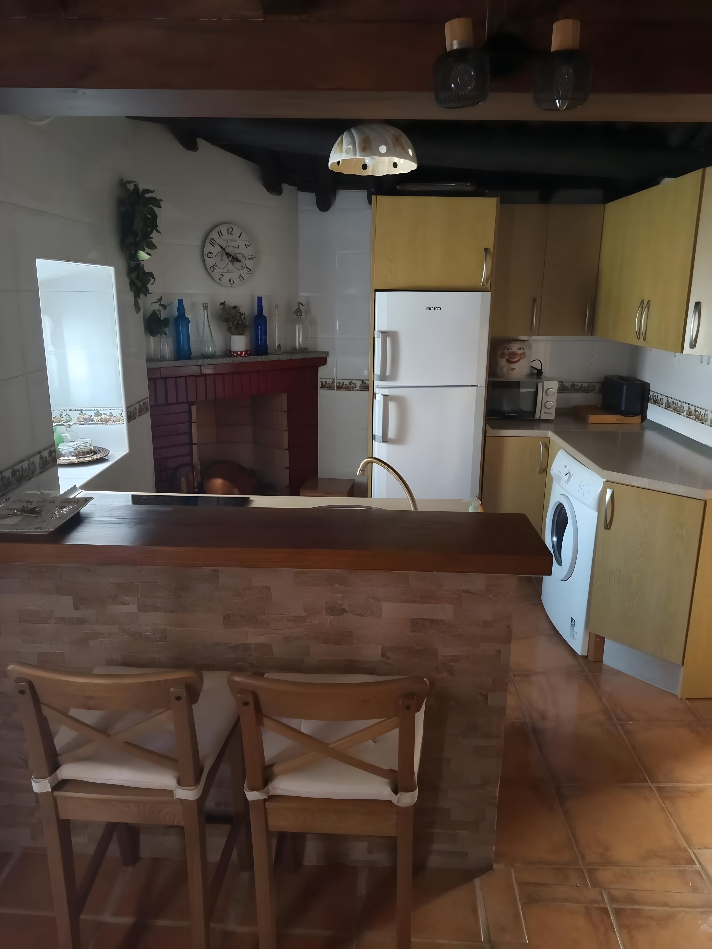A kitchen with a central island, wooden chairs, a washing machine, and a refrigerator.