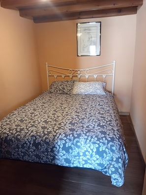 Een enkel bed met een metalen frame en een sprei met bloemenprint in een kamer met perzikkleurige muren en houten vloeren.