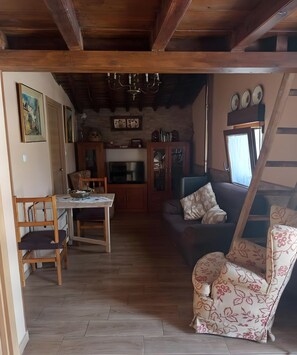 Een knus zithoek met een houten vloer, een bank, een gestreept fauteuil, een eettafel met stoelen, en een keuken op de achtergrond.