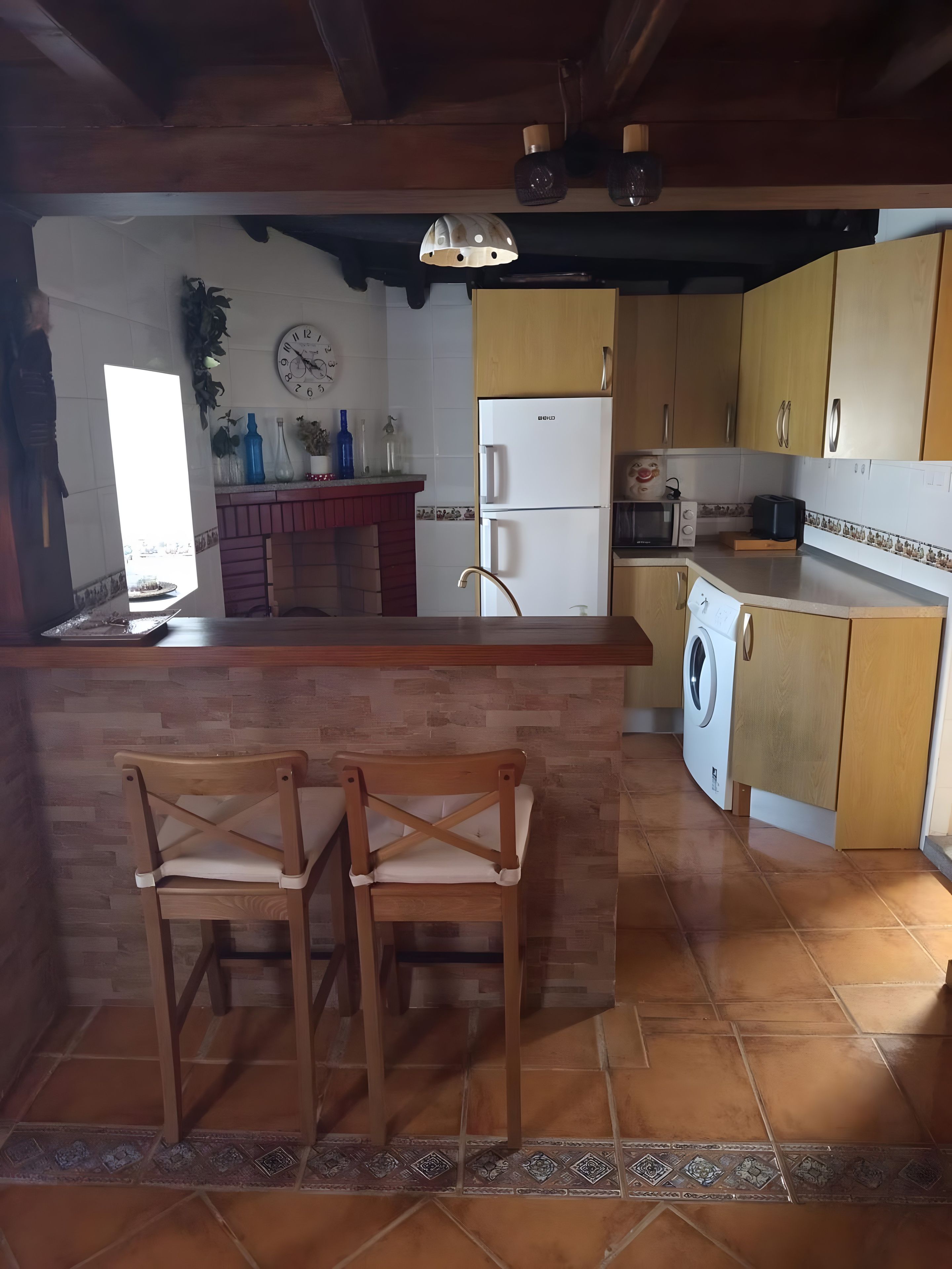 Una cocina con una isla central, sillas de madera, un refrigerador, una lavadora y un microondas.