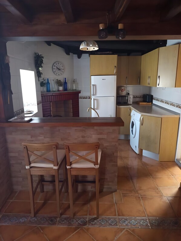 Una cocina con una isla central, sillas de madera, un refrigerador, una lavadora y un microondas.