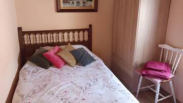 Una cama con colcha floral, cabecera de madera y un cuadro encima.