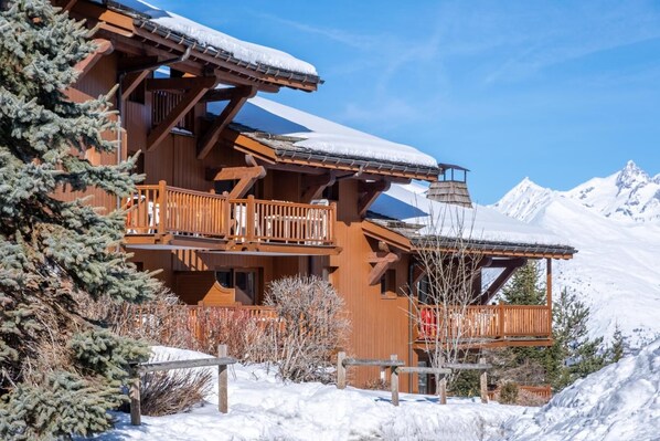 Una cabaña de madera con balcones, rodeada de montañas nevadas.