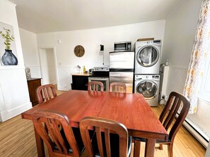 Una cocina compacta con una mesa y sillas de madera, un microondas, una lavadora y un reloj en la pared.