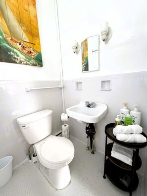 Un baño con inodoro, lavamanos y toallero con artículos de aseo.