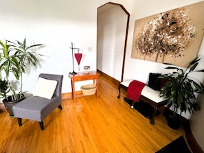 Una habitación con un sofá gris, una mesita de madera, una lámpara roja, un cuadro abstracto grande y dos plantas en macetas.