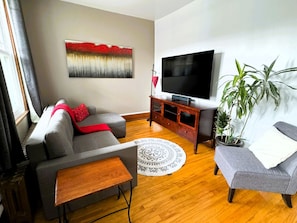 Una sala de estar con sofá, mesa de centro, televisor, aparador y una planta en maceta.
