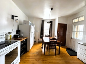 Cocina compacta con zona de comedor, piso de madera y ventana con cortinas.