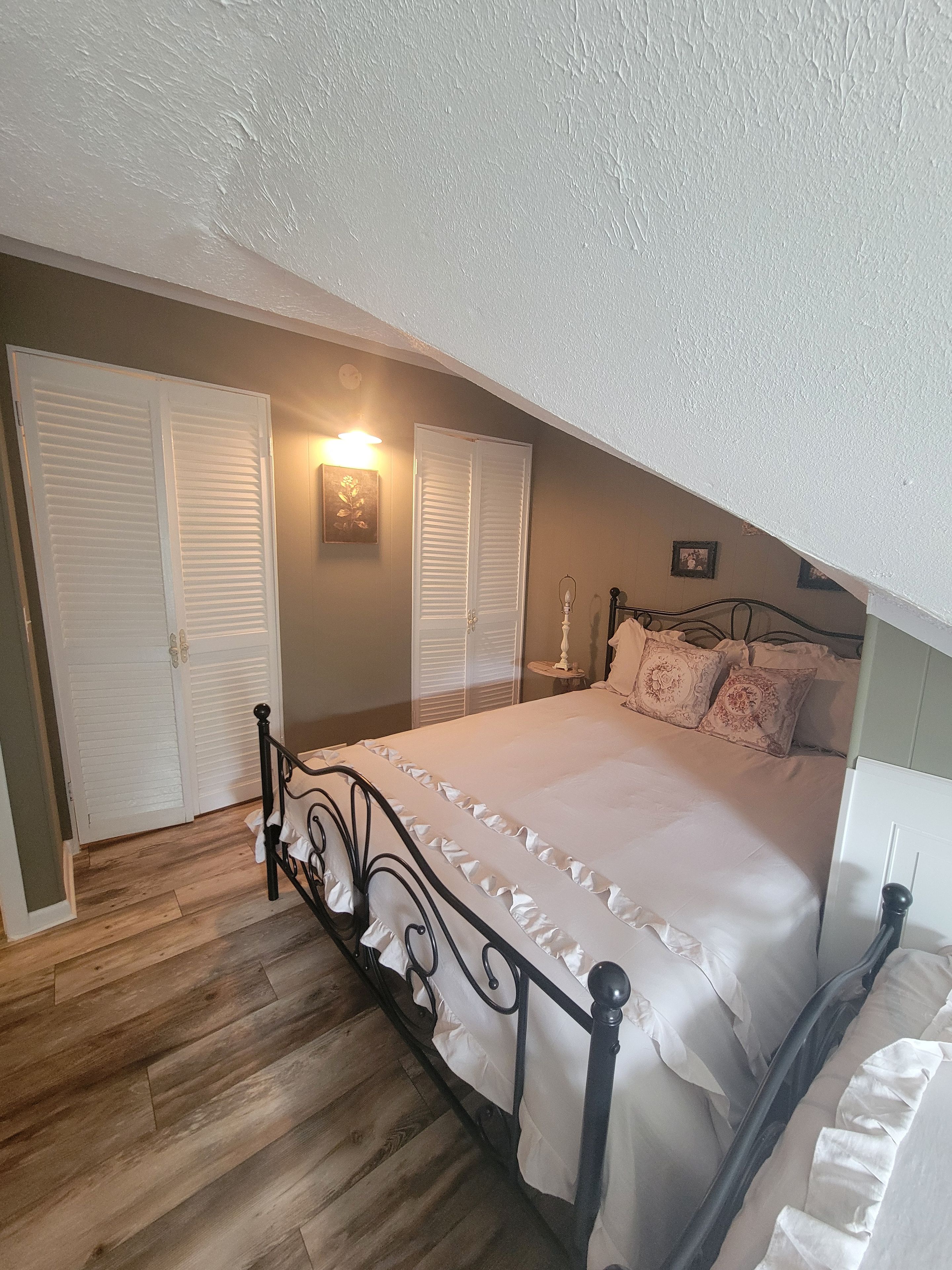 Quarto com cama, mesa de cabeceira, abajur e luminária na parede.