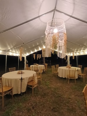 Una carpa con mesas y sillas redondas, un lámpara colgante y un banderín.