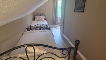 Un dormitorio con techo inclinado, una cama con cabecera decorativa, un cuadro enmarcado en la pared y una ventana con cortinas.
