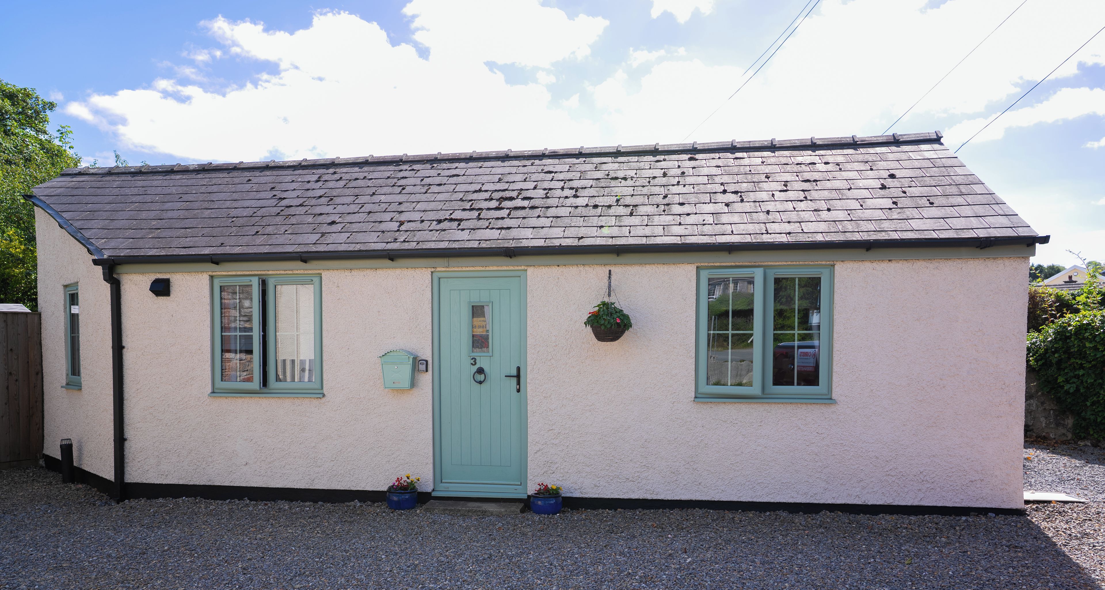 A small, single-story building with a sloped roof, a green door, and two windows.