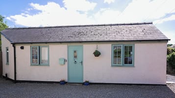 A small, single-story building with a sloped roof, a green door, and two windows.