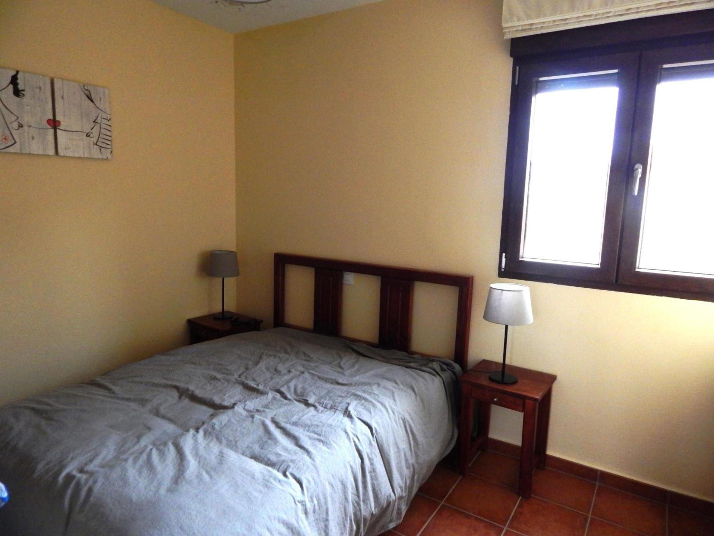 Un dormitorio con cama, dos mesitas de noche, una ventana y una obra de arte en la pared.