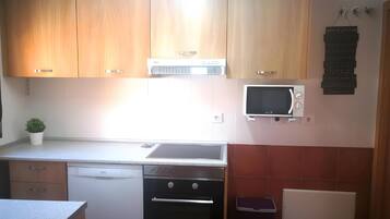 Una cocina con armarios de madera, microondas, lavavajillas y una pequeña planta en maceta.