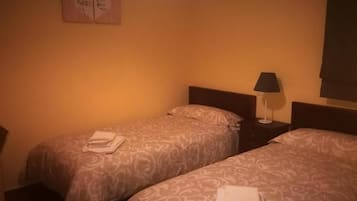 Habitación de hotel con dos camas, cada una con una colcha estampada y una toalla doblada. Hay una mesita de noche con una lámpara entre las camas.