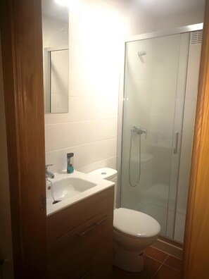 Et badeværelse med en glasvæg omkring bruseren, en hvid vask og et toilet.
